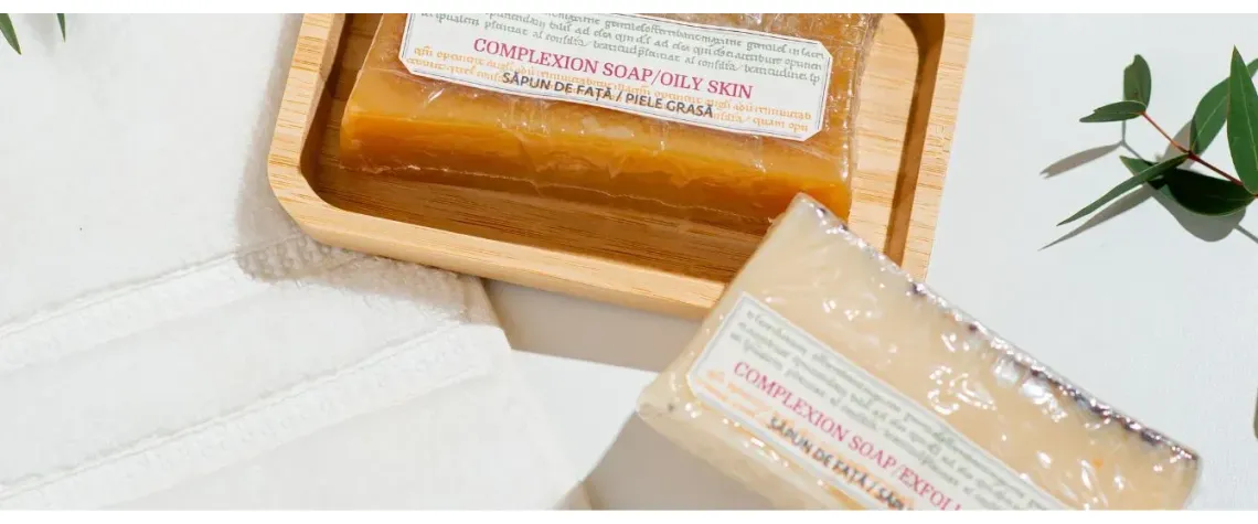 Căzi de săpun natural ambalate, așezate într-o tavă de lemn, pe o suprafață albă, sugerând produse cosmetice naturale.